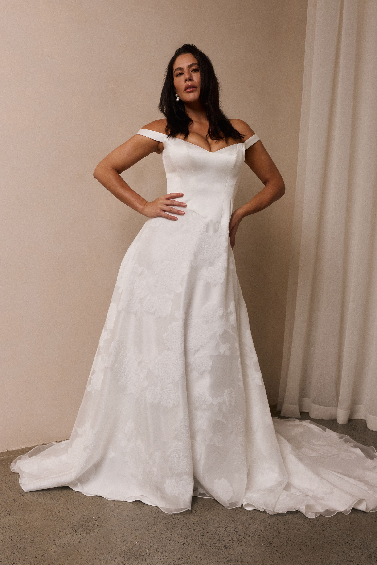 A woman wearing an off-the-shoulder white wedding dress with a fitted bodice and flowing skirt_L_