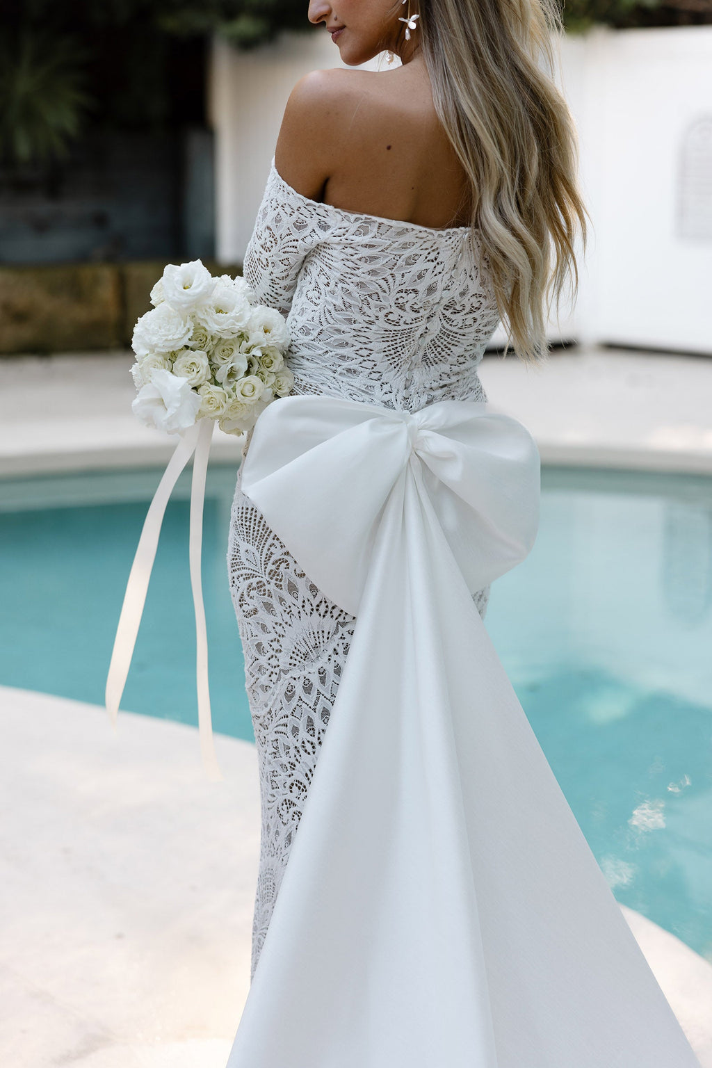 Woman in a lace wedding dress and bow holding a bouquet by a pool