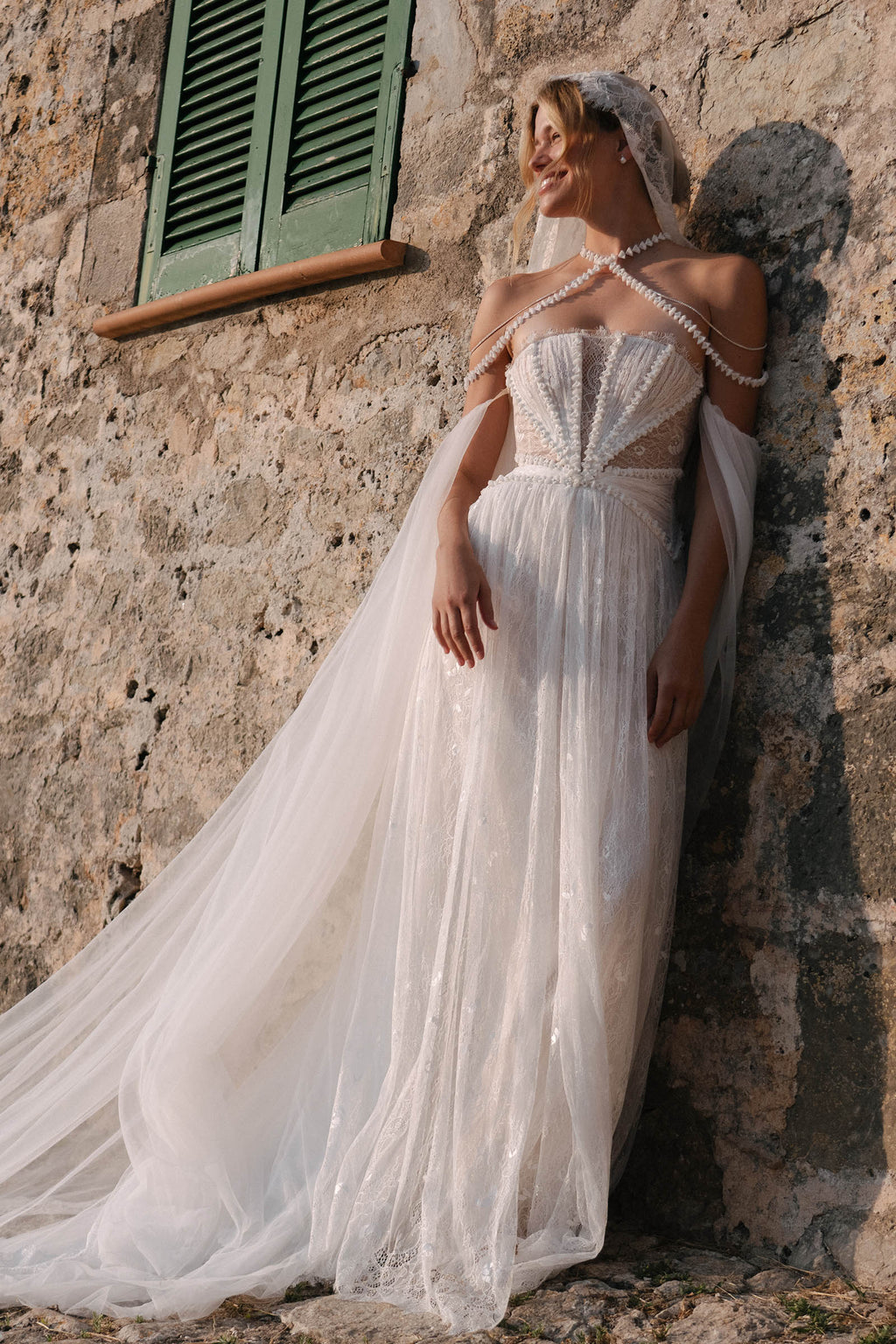 Woman in a lace wedding dress leaning against a stone wall_XS_