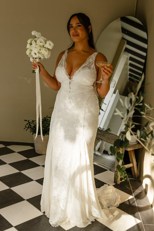 Woman in a V-neck lace wedding dress holding a bouquet