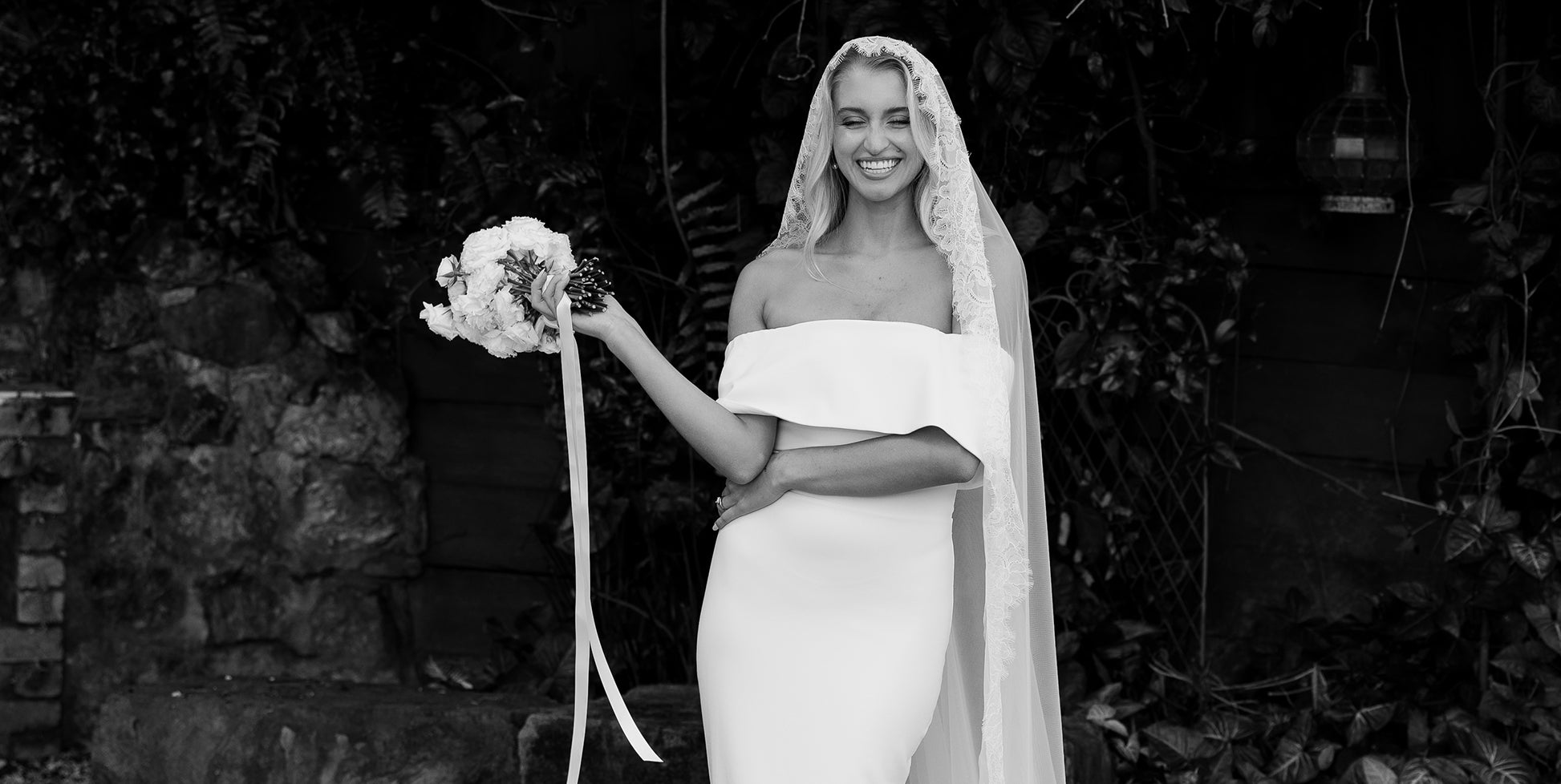 A bride wearing an off the shoulder wedding dress and lace veil.