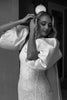 Black and white photo of a woman in a wedding dress and bridal cape adjusting her hair.