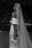 Bride in a wedding gown with a long veil holding a bouquet outdoors.