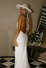 Woman in a low back lace wedding dress and a white hat, laughing.