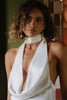 Woman wearing a white halter neck dress  and pearl earrings with a blurred background
