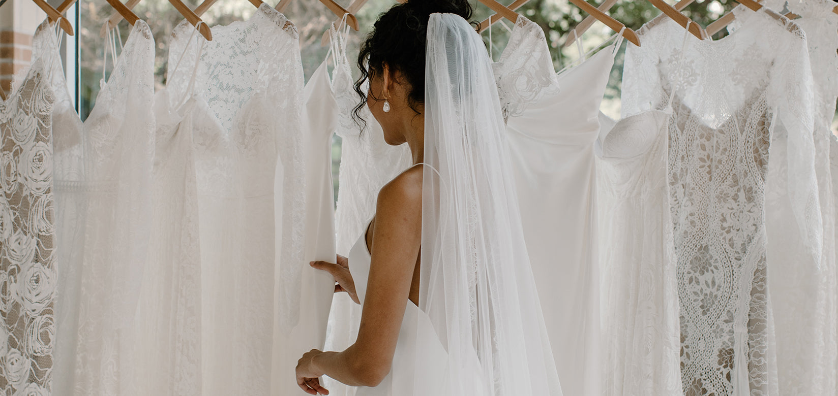 wearing wedding dress looking at rail of wedding dresses